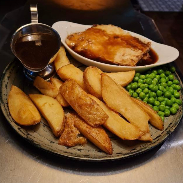 Steak and ale pie, with chunky chips, garden peas. and a gravy boat.